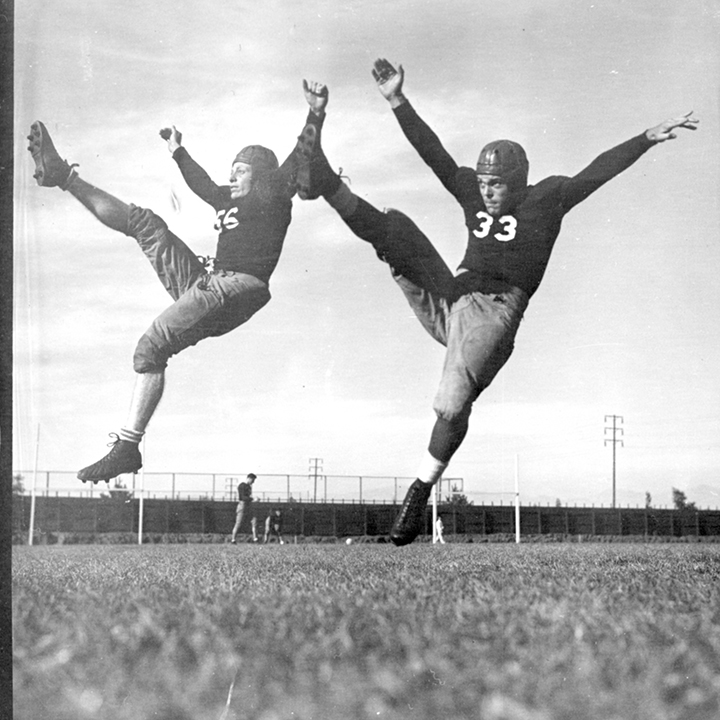 Two football players in a synchronized high kick with arms raised